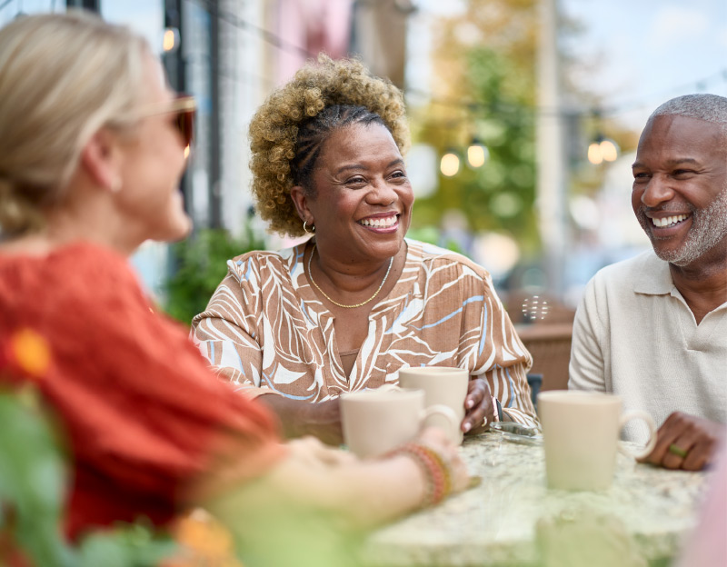 Married couple and husband having a cup of coffee smiling with friend at a street side table