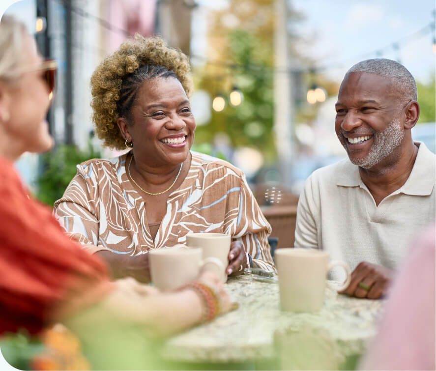 Married couple and husband having a cup of coffee smiling with friend at a street side table